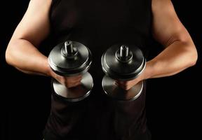 man in black clothes holds steel dumbbells in his hands, his muscles are tense photo