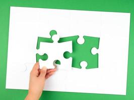 female hand puts empty white big puzzles on a green background photo