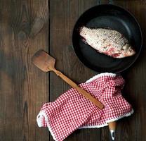 fresh crucian fish sprinkled with spices and lies in a black round pan photo