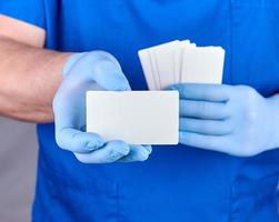 male doctor wearing blue latex gloves is holding a blank white paper business card photo