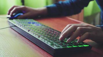 Young gamer plays a video game uses gaming illuminated keyboard.