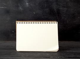 open spiral notebook with blank white sheets against a black chalk board photo