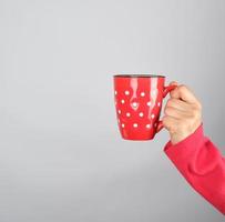 red ceramic cup in a female hand on a white background photo