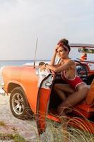 Sexy woman wearing red swimsuit in retro cabriolet car on the beach. photo