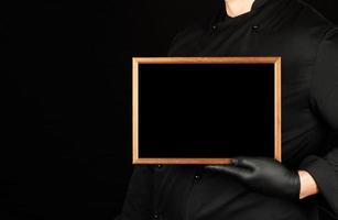 chef in black uniform and black latex gloves holds an empty wooden frame photo