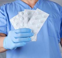 doctor in blue latex gloves holds pills in white paper packaging photo