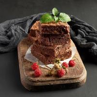 stack of baked square pieces of chocolate brownie cake on brown wooden cutting board photo