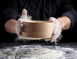 man sifts white wheat flour through a wooden sieve photo