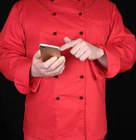 chef en uniforme rojo tiene en su mano un teléfono inteligente foto