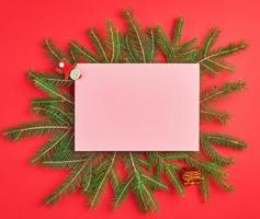 fondo de felicitación de navidad con una hoja rosa vacía y ramas verdes foto