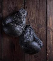 pair of very old shabby black leather boxing gloves hanging on a nail photo