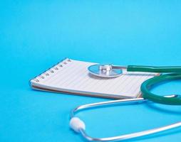 green medical stethoscope and empty paper notebook photo