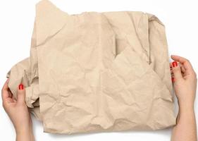 female hands hold crumpled brown paper on white background photo