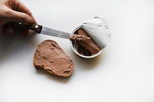 Meat pate in a jar on a white background. Spreading pate on bread with a knife. Meat pate, knife and bread. Delicious breakfast of pate. photo