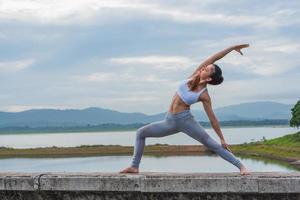 Young Asian woman doing Yoga exercise in beautiful lake with mountain background in the morning. photo