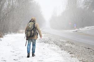 un hombre con una mochila grande camina por una carretera asfaltada suburbana foto