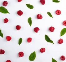 red ripe raspberries and green leaves scattered on a white background photo