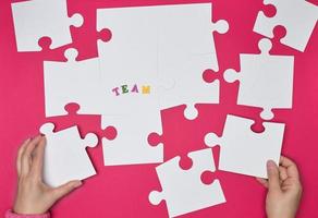 female hand puts white big puzzles on a red background photo