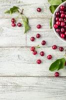 tazón blanco de cerezas dulces frescas con hojas en gotas de agua sobre fondo de madera foto