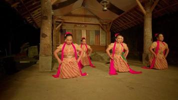 Javanese people dance together in an orange dress with a green scarf while the festival begins inside the village video