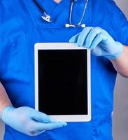 doctor in blue uniform and latex sterile gloves holding an electronic tablet with a blank black screen photo