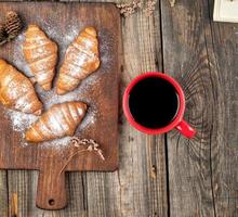 ceramic red cup with black coffee and wooden cutting board with baked croissants photo