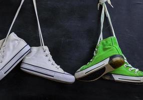 two pairs of used textile shoes hang on a black background, close up photo