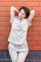 Cheerful woman in home wear pajama outdoor brick wall background emotions - sleepwear and homewear concept photo