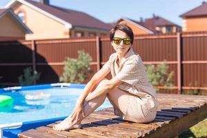 Portrait of pretty young woman in pajama sitting near inflatable swimming pool - summer and country life concept photo