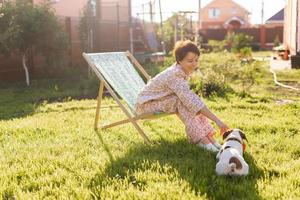 Young woman in pajama is resting in chair on a green lawn on sunny summer day - village and country life photo