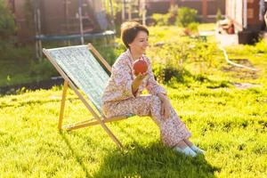 mujer joven en pijama está descansando en una silla en un césped verde en un día soleado de verano - vida de pueblo y campo foto