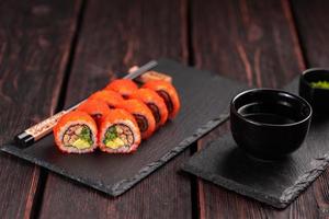 California sushi roll with eel, cucumber and tobiko caviar served on black board close-up - Japanese food photo