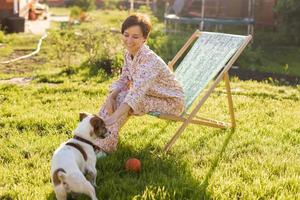 Young woman in pajama is resting in chair on a green lawn on sunny summer day - village and country life photo