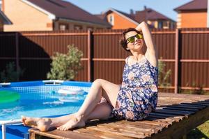 Portrait of pretty young woman in pajama sitting near inflatable swimming pool - summer and country life concept photo