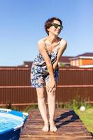 Portrait of pretty young woman in pajama sitting near inflatable swimming pool - summer and country life concept photo