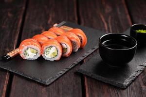 sushi roll philadelphia con salmón y pepino con aguacate y queso crema sobre fondo negro. menú de sushi concepto de comida japonesa foto