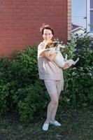 Young woman wearing homewear holding jack russell terrier dog near his house on backyard - pet owner and animal photo