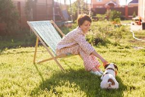 Young woman in pajama is resting in chair on a green lawn on sunny summer day - village and country life photo