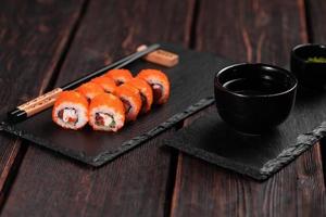 Sushi roll with shrimp and red pepper and tobiko caviar with salad served on black board close-up - Japanese food photo