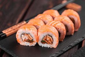 Sushi roll maguro with salmon, smoked eel, avocado and tobiko on black board close-up. Sushi menu. Japanese food. photo