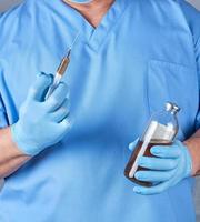 médico con uniforme azul y guantes estériles de látex sosteniendo una jeringa foto