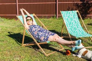 mujer joven en pijama está descansando en una silla en un césped verde en un día soleado de verano - vida de pueblo y campo foto