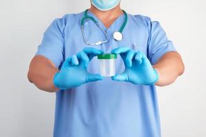 doctor in blue uniform and latex gloves is holding an empty plastic container photo