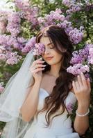 young girl bride in a white dress in a spring forest in lilac bushes photo