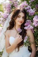 young girl bride in a white dress in a spring forest in lilac bushes photo