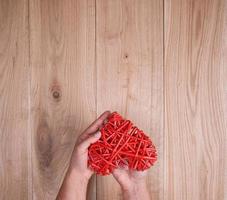 corazón rojo en mano humana sobre fondo amarillo de madera de tablones de roble foto