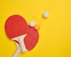 un par de raquetas de tenis de madera para ping pong y pelotas de plástico sobre un fondo amarillo foto