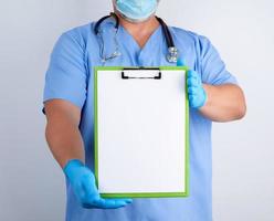 médico con uniforme azul y guantes de látex sostiene un soporte verde para hojas de papel foto