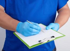 doctor in blue uniform and latex gloves holds a green holder for sheets of paper photo