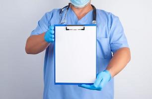 médico con uniforme azul y guantes de látex sostiene un soporte verde para hojas de papel foto